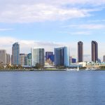 Panoramic photographic image of the San Diego skyline during the day. Ocean (harbor) in the foreground, with office buildings in the background. Blue skies. Image used pursuant to license.