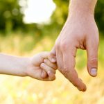 Photo image. Close-up of a child's small arm and hand grasping onto the hand of an adult. The image conveys the importance of considering children and the need to protect them from the costs of probate and lack of experienced estate planning.