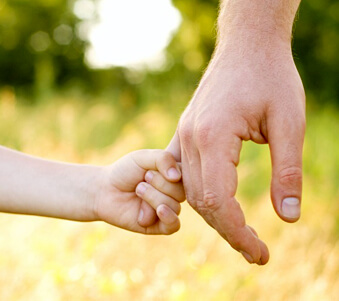 Photo image. Close-up of a child's small arm and hand grasping onto the hand of an adult. The image conveys the importance of considering children and the need to protect them from the costs of probate and lack of experienced estate planning.