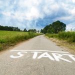 Photograph image of a road. The road is cutting between a countryside location. The word "start" is written on the road in white paint or white chalk. The image connotes a feeling of being lost, but now being on the right road. Hopeful and helpful.